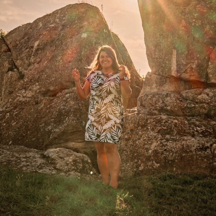 Angelika Steiden von Balance Boost steht neben großen Felsen, hinter ihr erstrahlt die Sonne